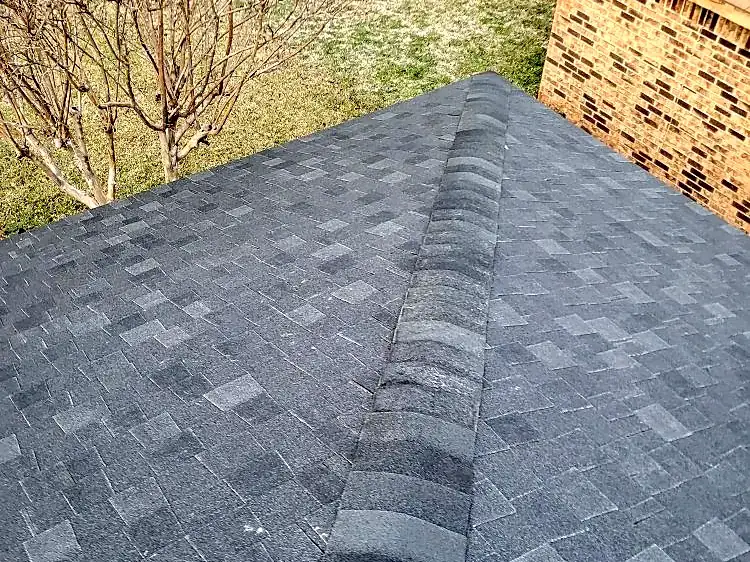 Ridge cap shingles finished neatly where the roof meets a brick wall